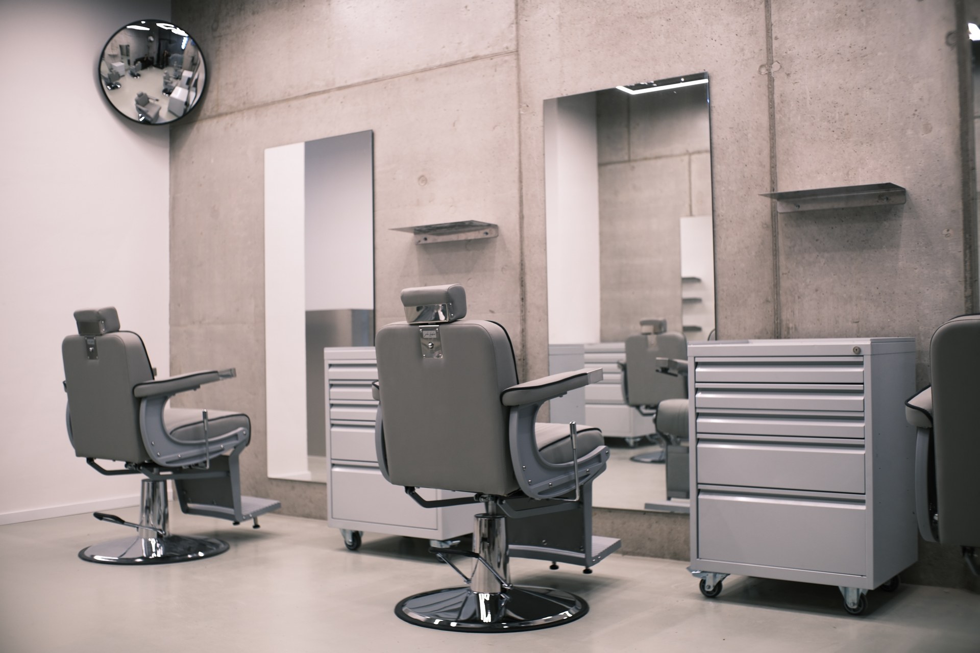 Interiér Ritual Barber Studia: šedá barberská křesla před betonovou stěnou se zrcadly